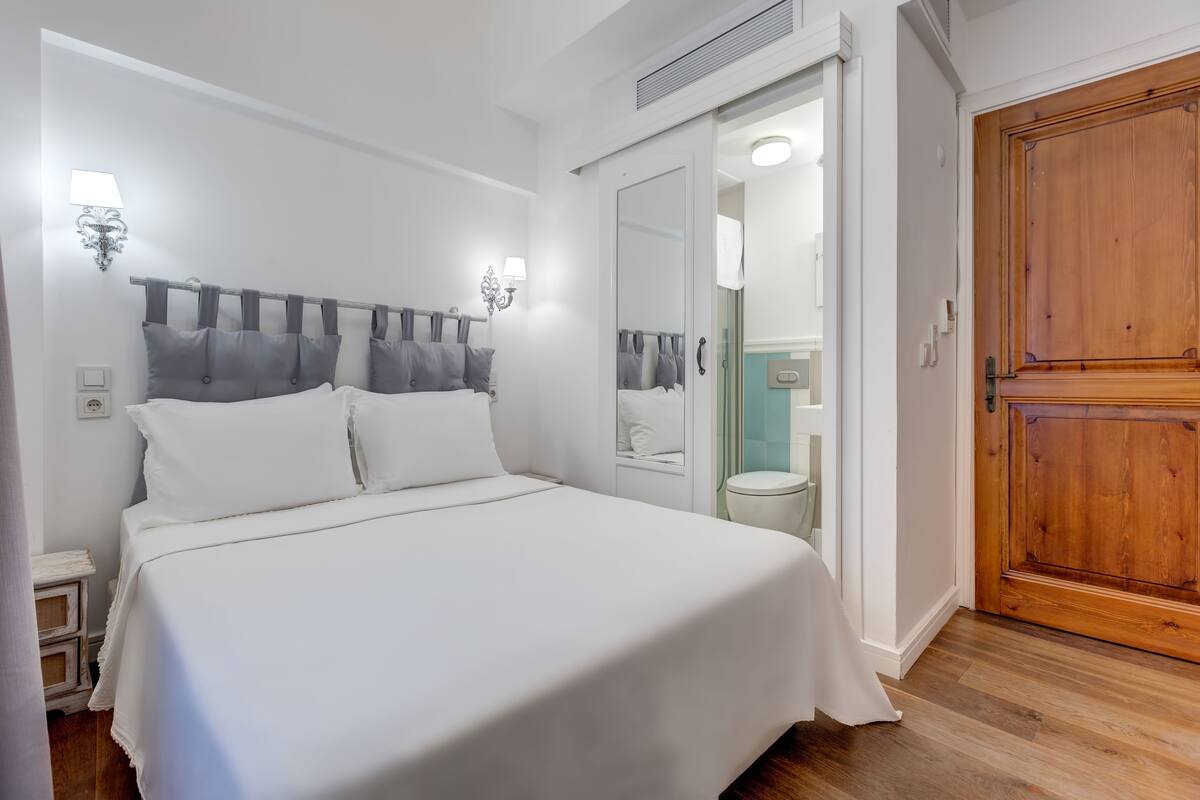 A bedroom with a large bed, a wooden wardrobe, and a bathroom visible through an open door.
