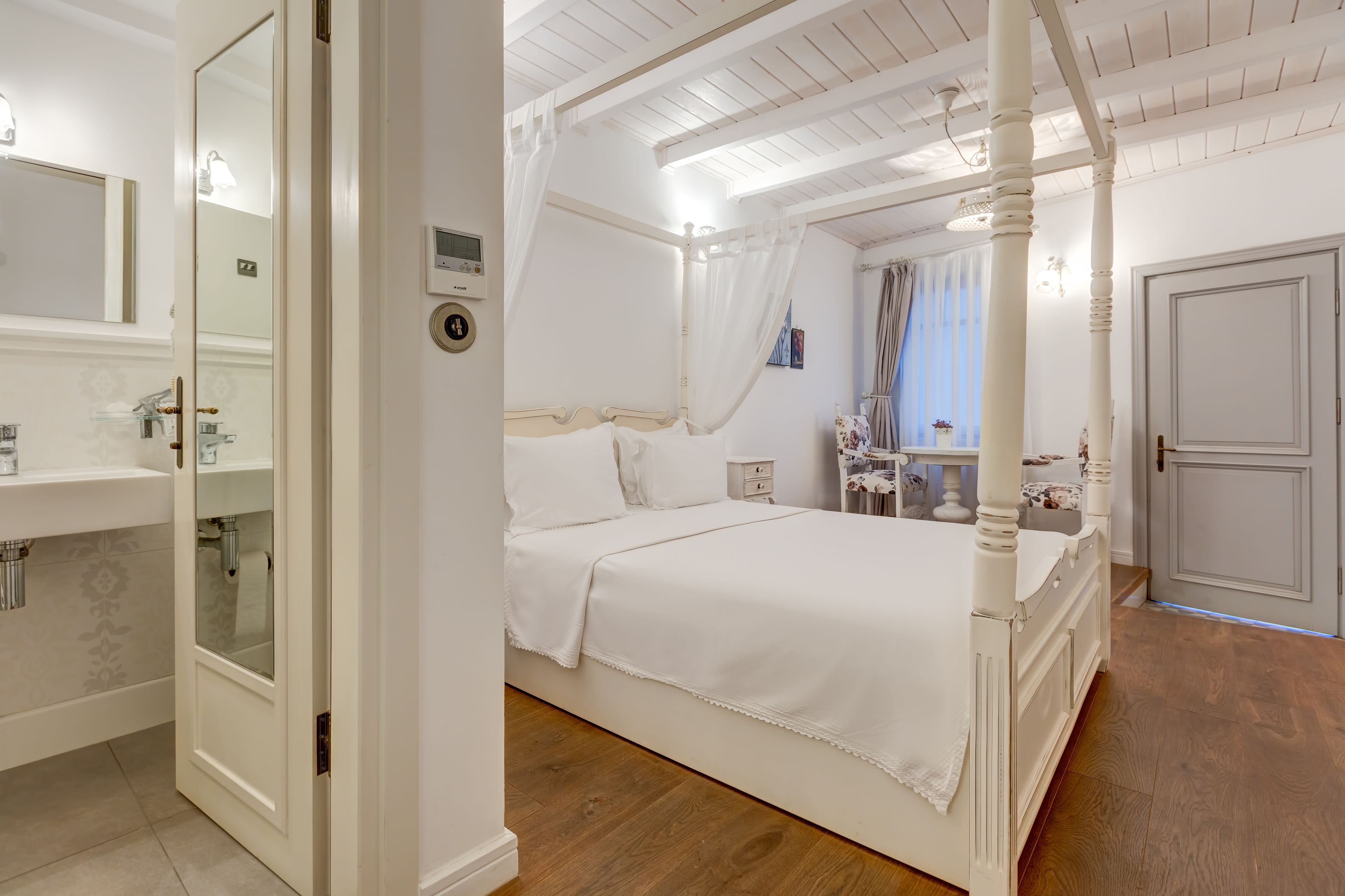 A bedroom with a four-poster bed, a bedside table, a nightstand, and a window with curtains.