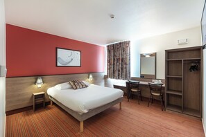 A hotel room with a bed, desk, chair, wardrobe, and a painting on the wall.