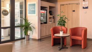 A reception area with a coffee machine, two red chairs, a potted plant, and a sign that reads "Simplement bien à l'Accueil". - ACE Hôtel Chartres (Le Coudray)