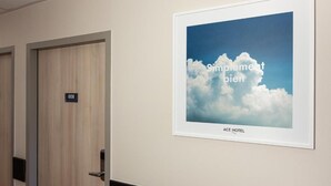 A hotel room with a door labeled '008' and a framed picture on the wall with the text 'Simpement bien' and 'ACE HOTEL'.