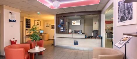 A hotel reception area with a counter, seating, and a plant.