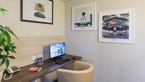 A hotel reception desk with a computer, phone, and framed pictures on the wall. - ACE Hôtel Chartres (Le Coudray)