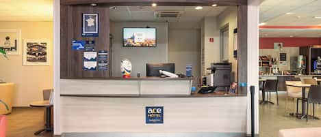 A hotel reception area with a modern design, a reception desk, a television screen, and various informational posters.
