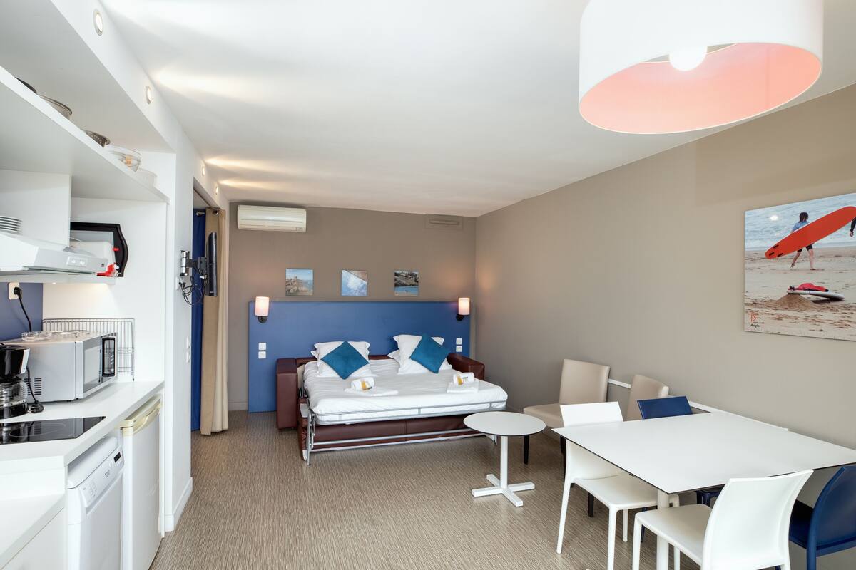 Une chambre d’hôtel comprenant un lit, une table à manger, un coin cuisine avec un four à micro-ondes et un luminaire au plafond.