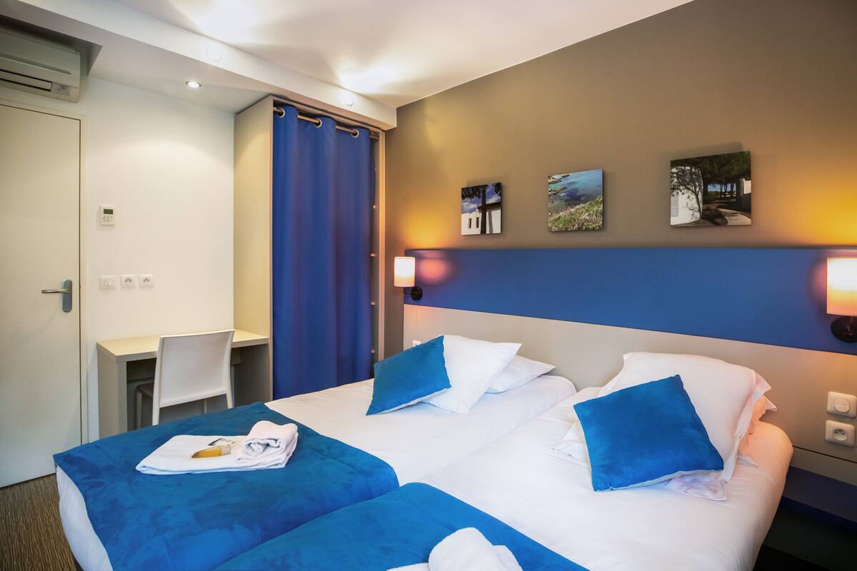Une chambre d’hôtel avec un lit, deux draps bleus, un bureau et une chaise.