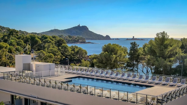 Une piscine sur le toit, agrémentée de chaises longues, offrant une vue dégagée sur la mer et un paysage montagneux en toile de fond.