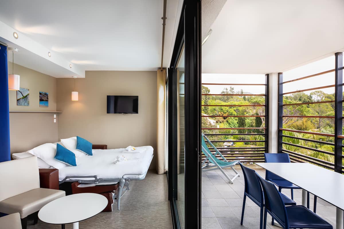 Une chambre d’hôtel moderne, équipée d’un lit, d’un canapé, d’une table et d’un balcon offrant une vue sur la verdure.