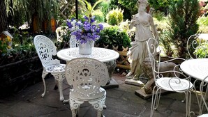 Une terrasse extérieure avec des chaises et des tables en métal blanc, une statue et diverses plantes.