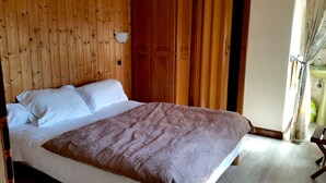 Une chambre à coucher avec une tête de lit en bois, un lit avec une literie blanche et marron, une table de chevet et une fenêtre avec des rideaux.