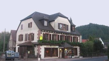 Ein traditionelles Gebäude mit Satteldach, einem zentralen Eingang mit Beschilderung und einem kleinen Balkon.