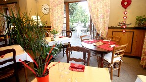 Un espace repas avec des tables préparées pour deux personnes, des chaises en bois et une plante en pot.