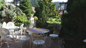 Une terrasse extérieure avec des meubles en métal blanc, une nappe colorée et une statue.