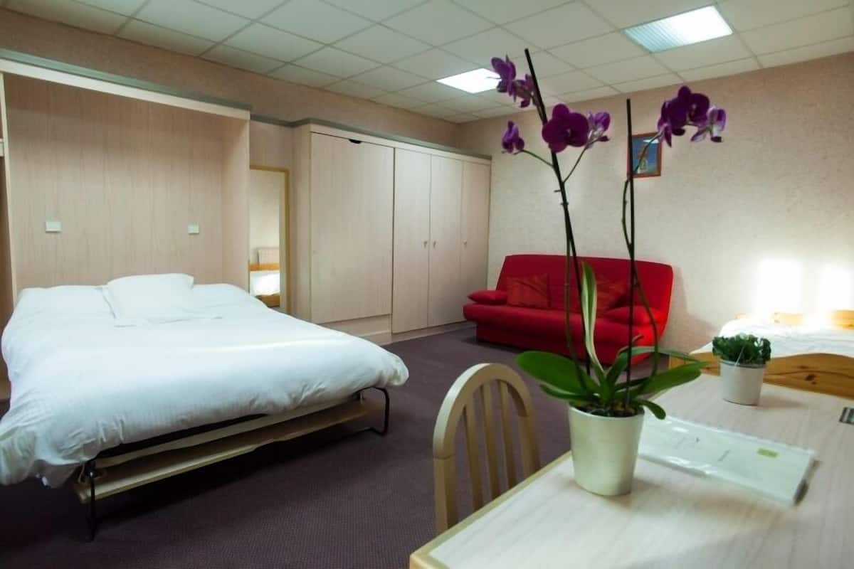Una habitación de hotel con una cama, un sofá rojo, una mesa con una planta y una pequeña planta en maceta sobre la mesa.