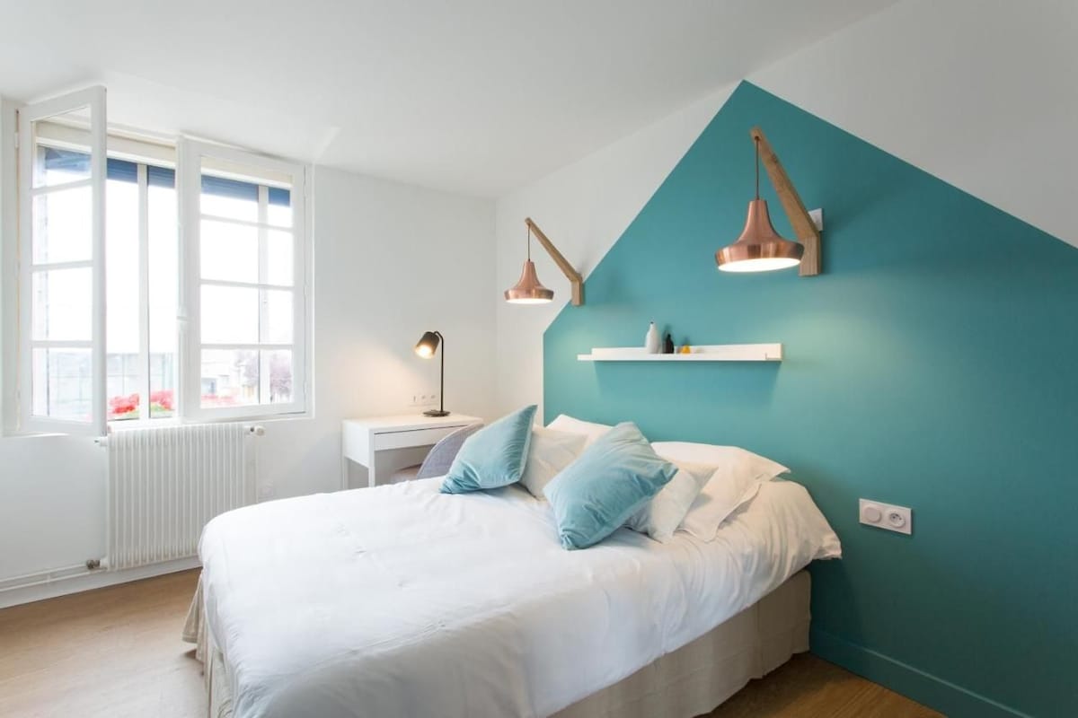 A bedroom with a bed, a nightstand, a lamp, a window, and a teal accent wall.
