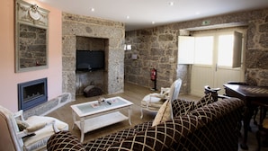 Un salon avec des murs en pierre, une cheminée, un téléviseur, un canapé, une table basse et une porte avec une fenêtre.
