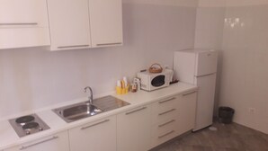 Una cocina moderna con armarios blancos, un lavamanos de acero inoxidable, un microondas y un refrigerador pequeño.