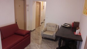 Una habitación con un sofá rojo, un sillón beige y una pequeña mesa con una máquina de escribir y libros.