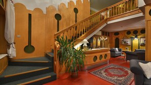 A wooden staircase with a railing, a living area with a sofa and a rug, and a potted plant. - Hotel Loredana (Livigno)