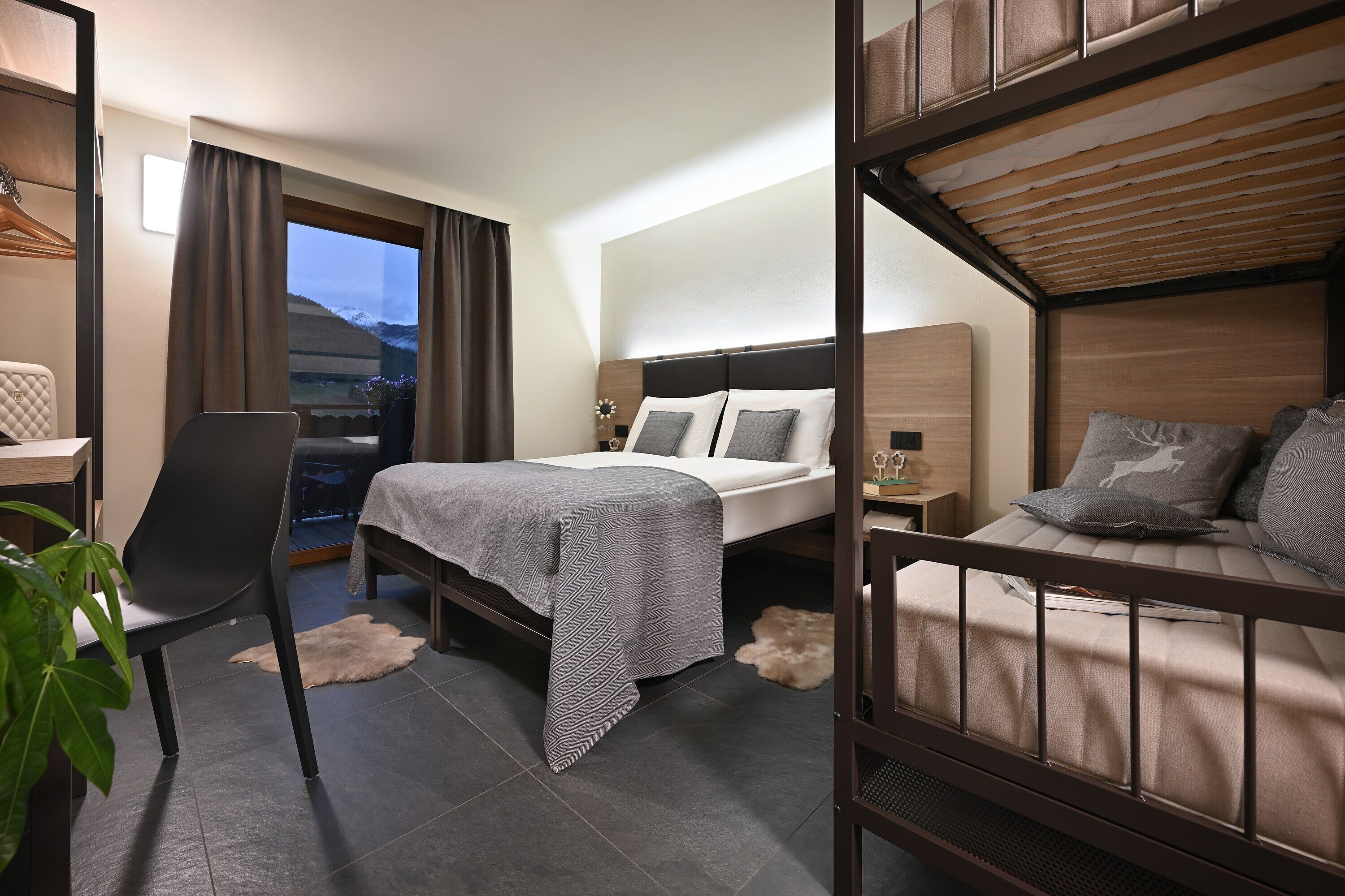 A hotel room with a bed, a desk, a chair, and a view of the mountains.