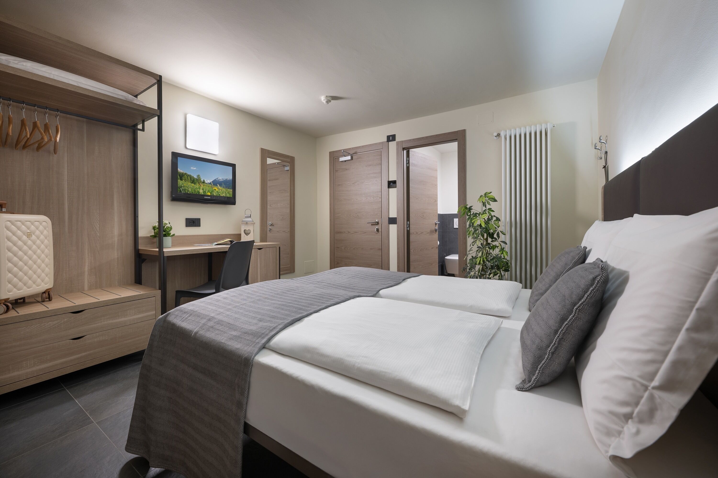 A modern hotel room with a bed, desk, and wardrobe.