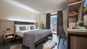 A modern hotel room with a large bed, a desk, a chair, and a view of the outdoors. - Hotel Loredana (Livigno)