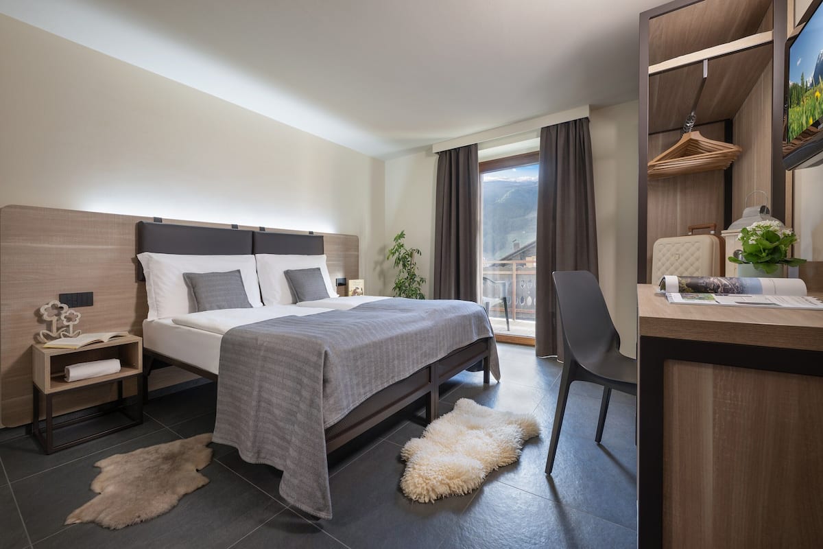 A modern hotel room with a large bed, a desk, a chair, and a view of the outdoors.