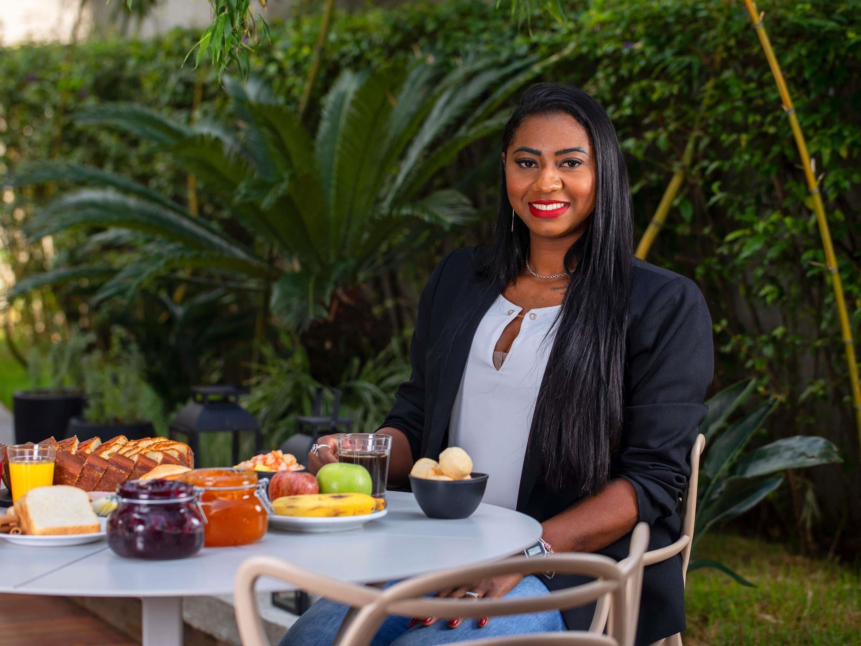 A person seated at an outdoor table with breakfast items, surrounded by lush greenery.
