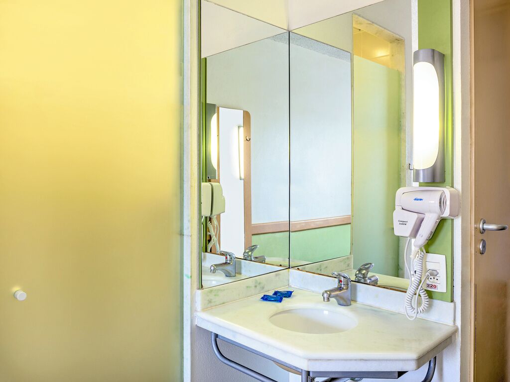 Une salle de bain équipée d’un lavabo, d’un miroir et d’un sèche-cheveux fixé au mur.