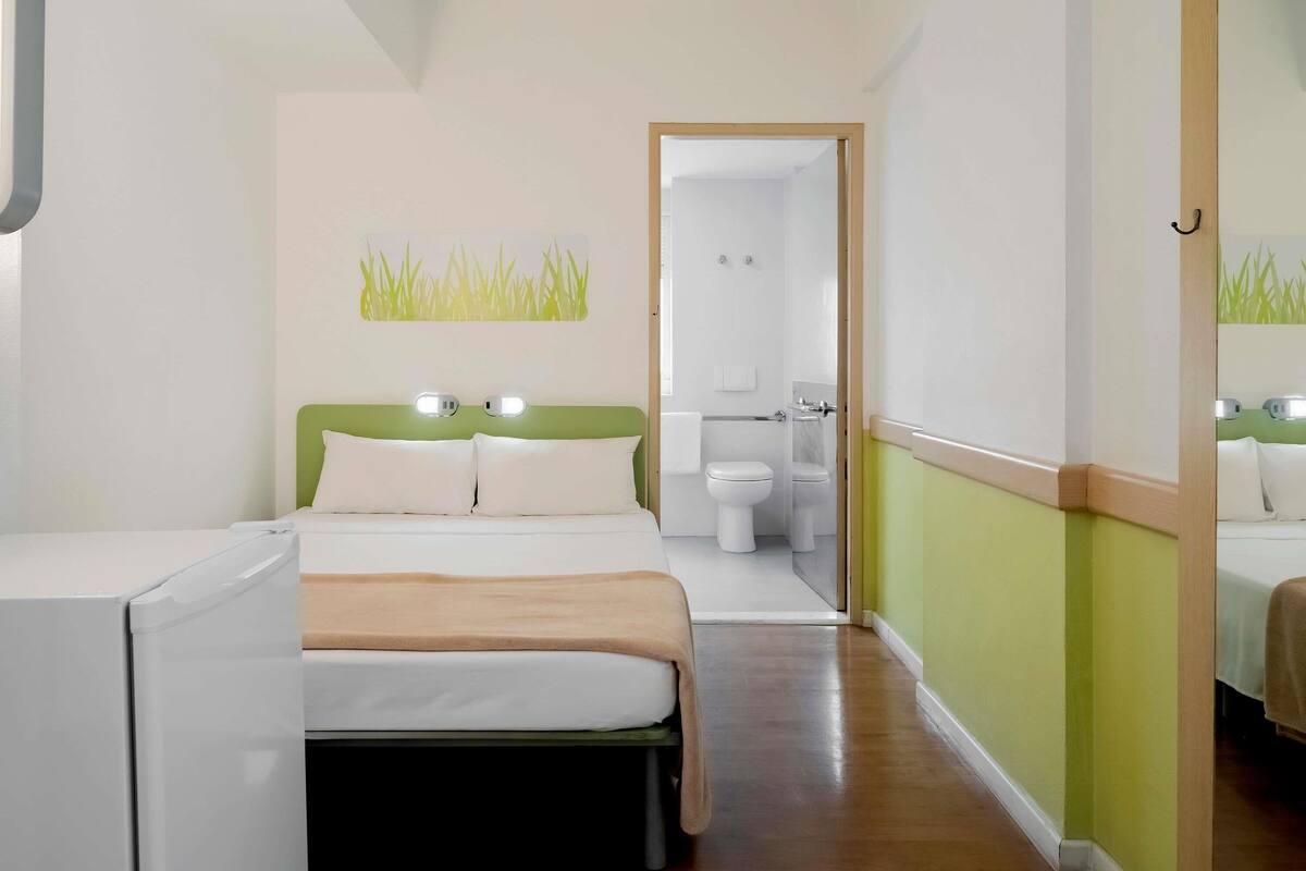 Une chambre d’hôtel comprenant un lit, une table de chevet, un miroir, des toilettes et un espace douche.