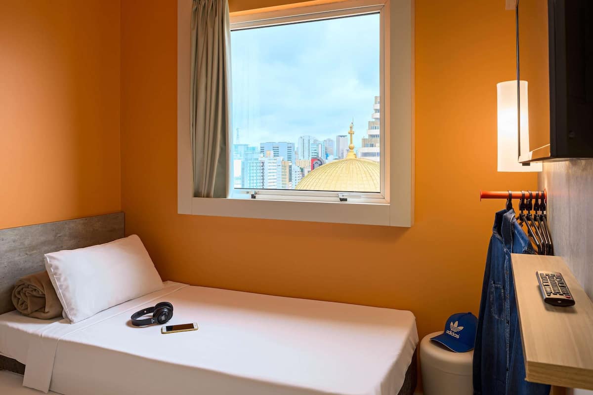 Une chambre d’hôtel avec un lit, une fenêtre donnant sur la ville, un bureau avec une lampe et une chaise.
