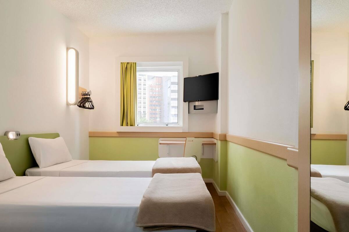 Une chambre d’hôtel avec deux lits, une télévision, une fenêtre avec des rideaux et une vue sur les bâtiments.