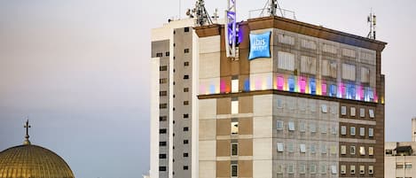 A high-rise hotel with a prominent "Ibis" sign, multiple floors, and a dome structure in the background.