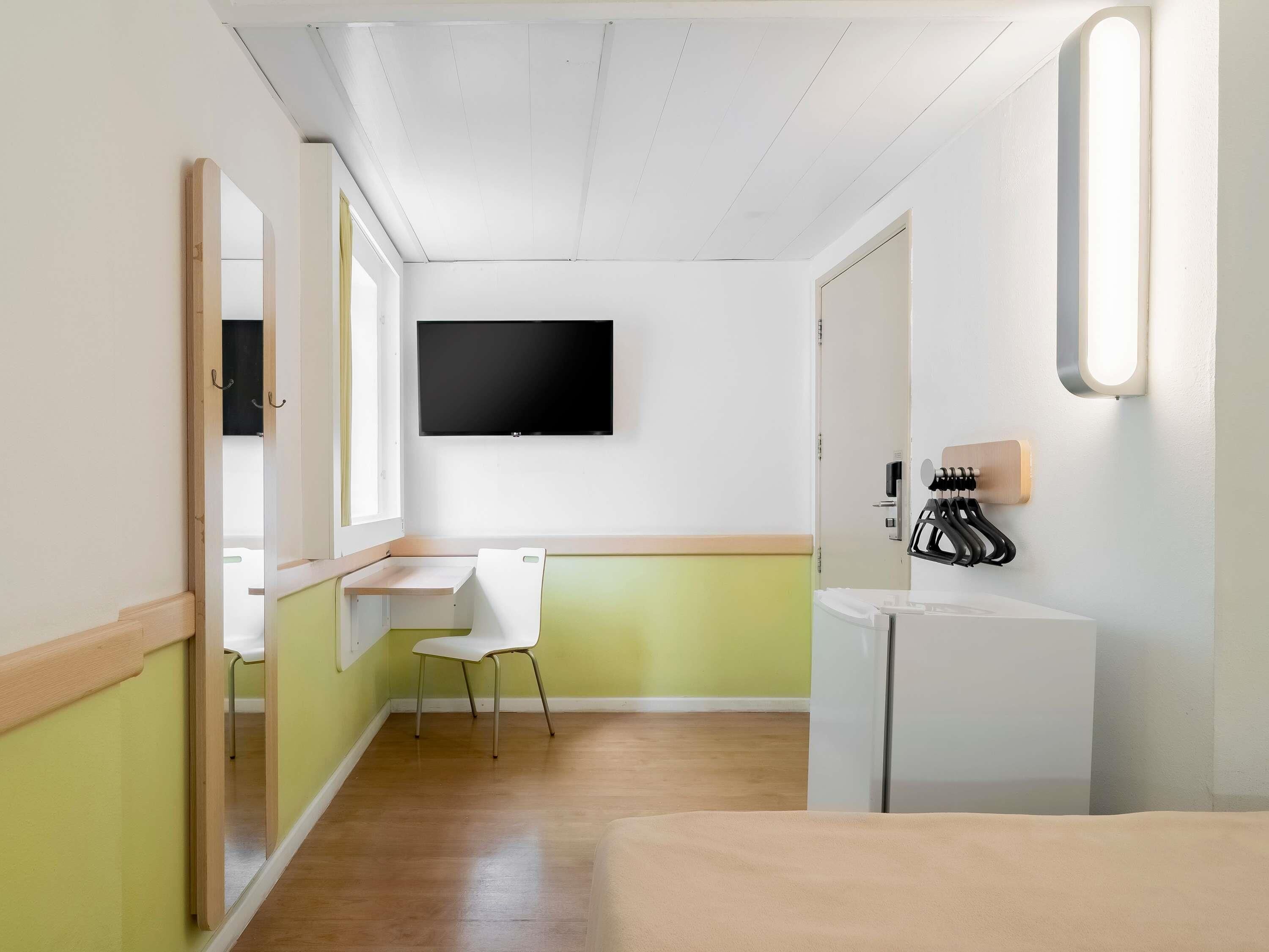 A hotel room with a bed, a desk, a chair, a television, and a mirror.