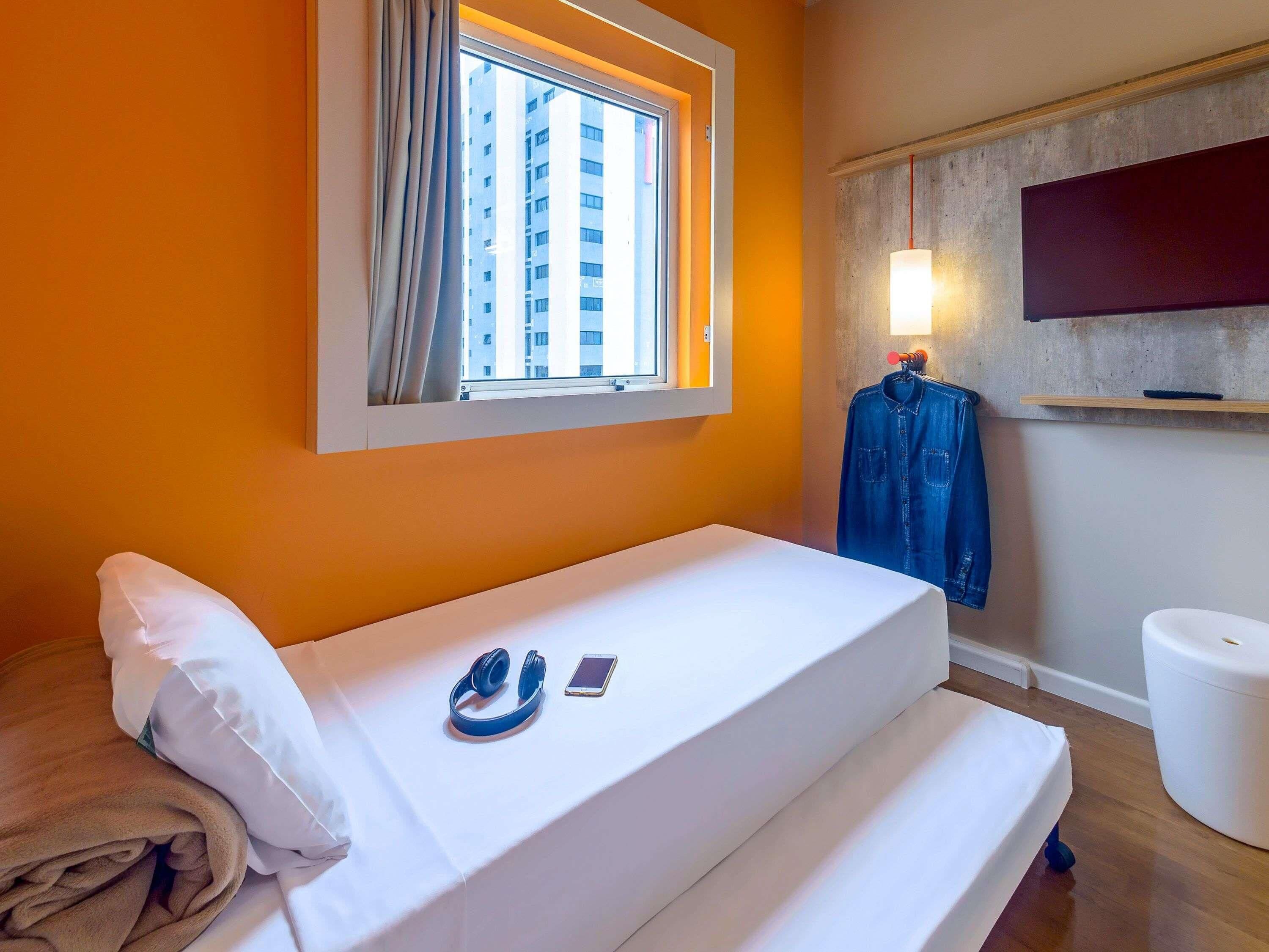 Habitación de hotel con cama, ventana con cortinas, televisión montada en la pared y piso de madera.