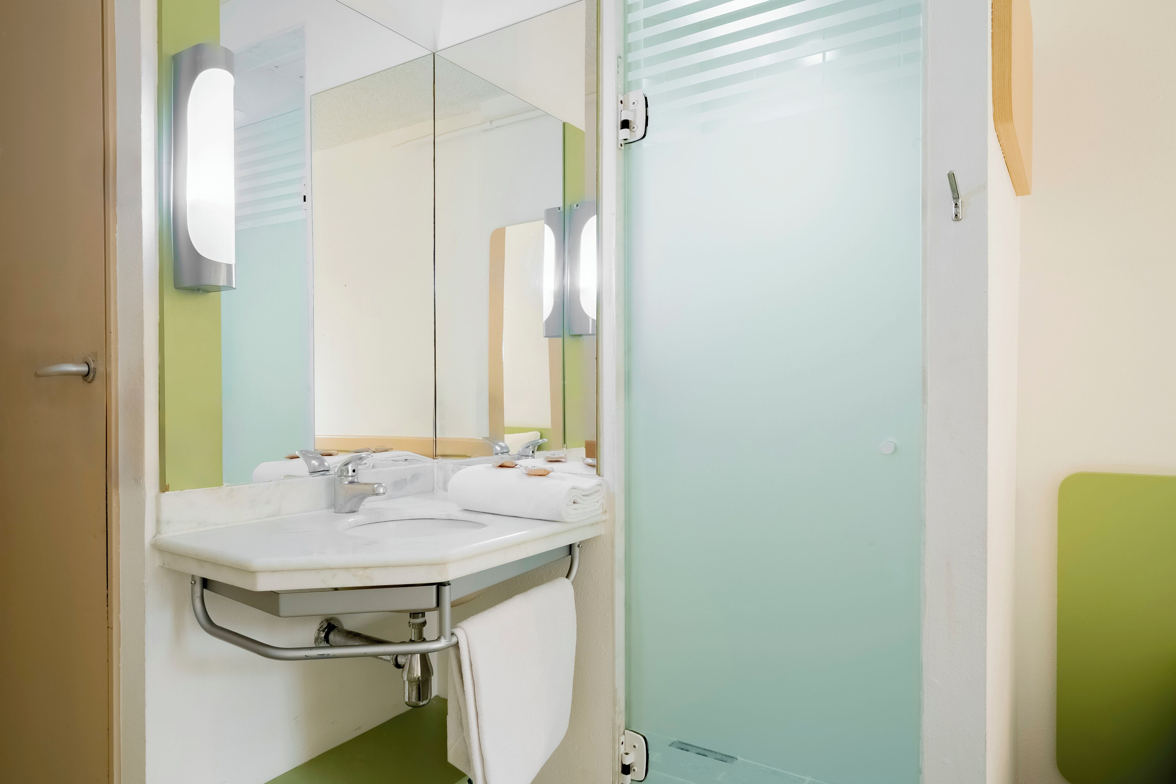 Un baño con lavamanos blanco, espejo y paredes verdes.
