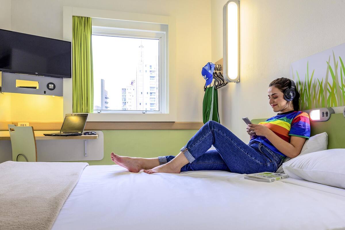 Hotelkamer met een bed, bureau met een laptop, flatscreen televisie en raam met gordijnen.