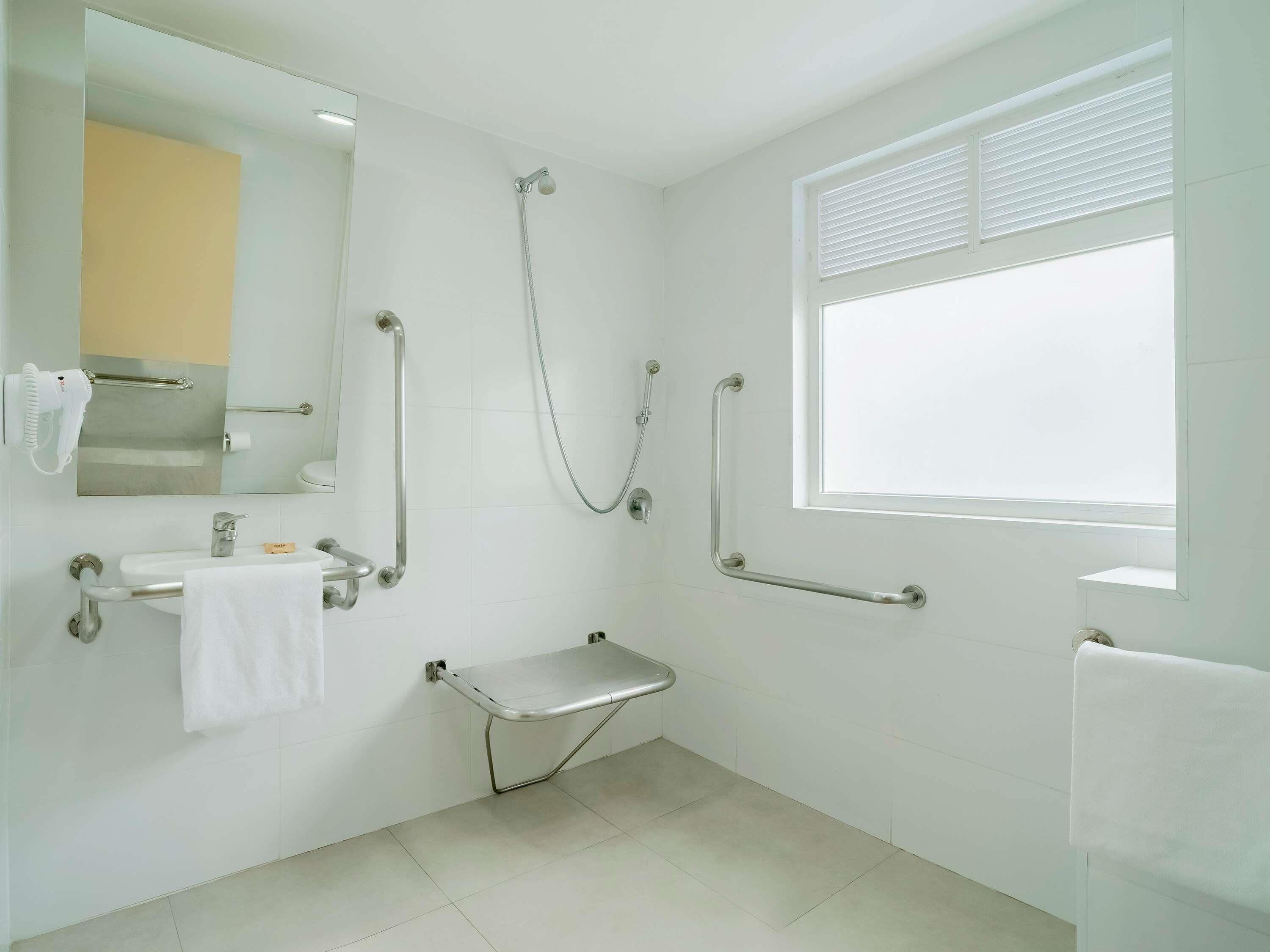 A modern bathroom with a shower, grab bars, a sink with a towel, and a window.
