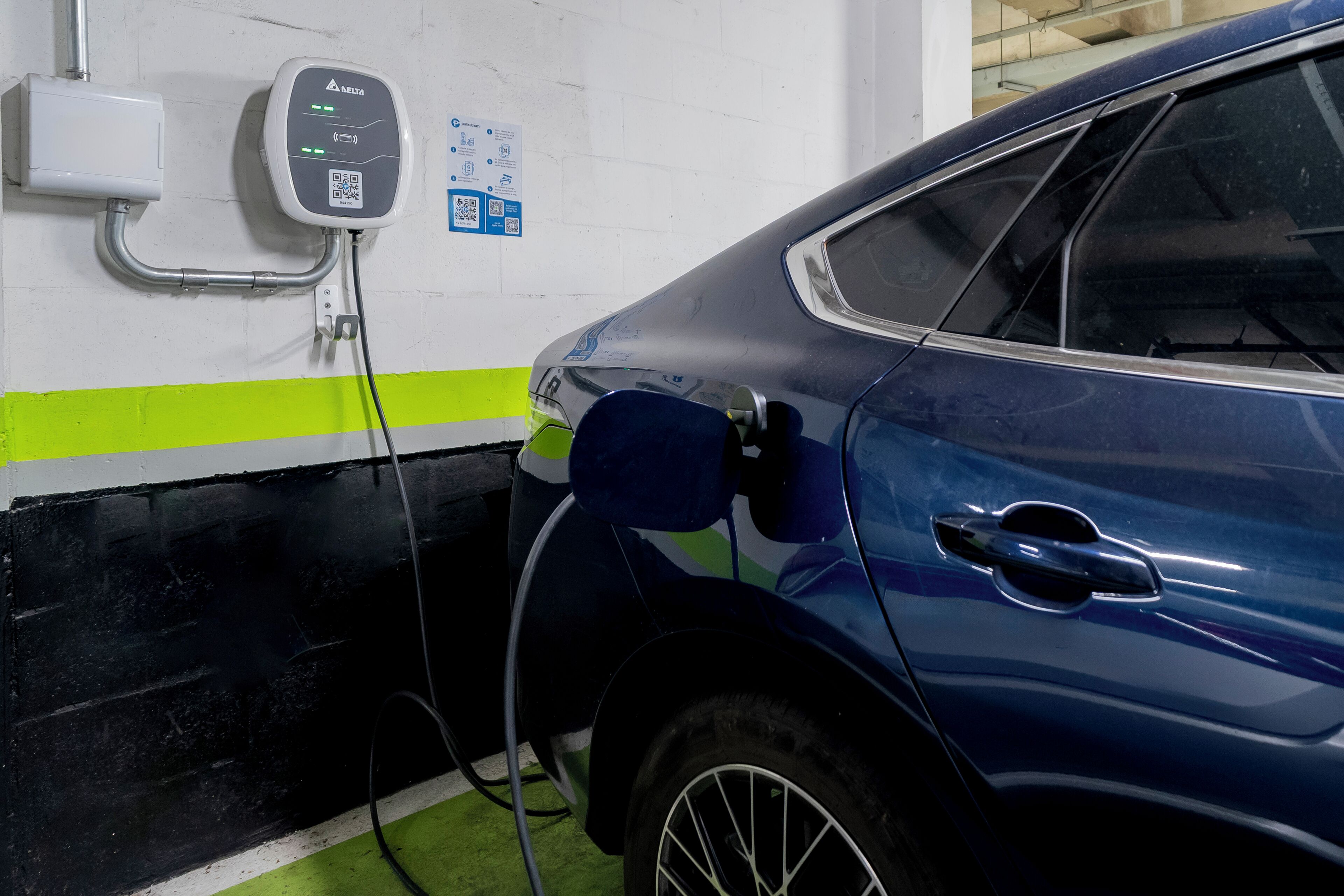 Un coche azul estacionado en una estación de carga con un código QR y una pantalla digital.