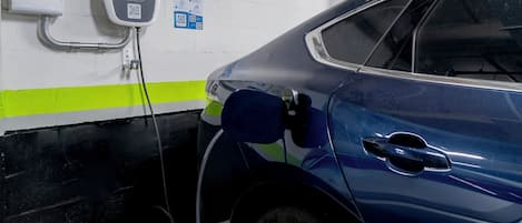 Un coche azul estacionado en una estación de carga con un código QR y una pantalla digital.