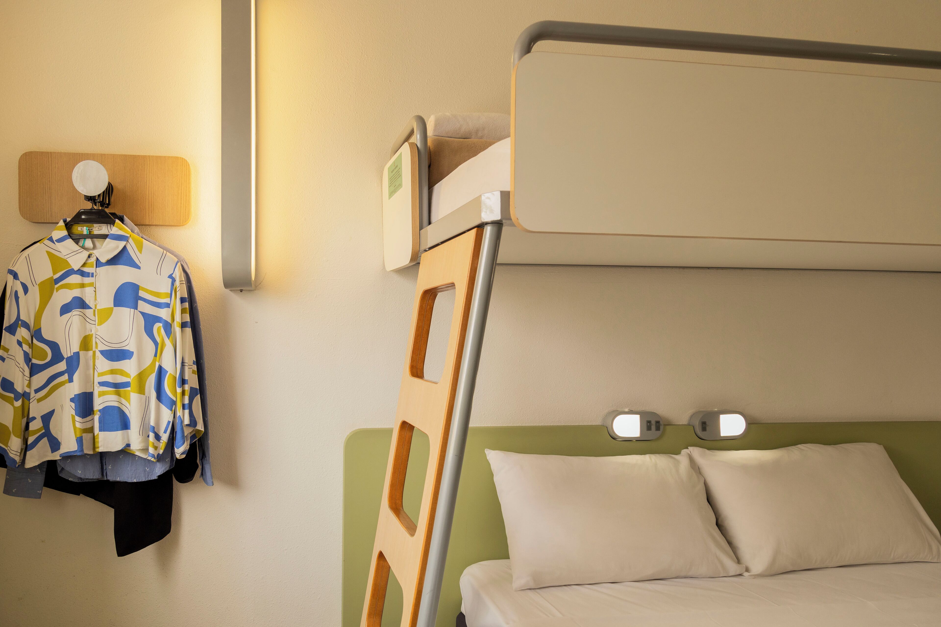 A bunk bed with a wooden headboard, a hanging coat rack with a colorful jacket, and two bedside tables with lamps.