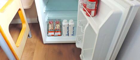 Un refrigerador con un estante que contiene latas, botellas y alimentos envasados.