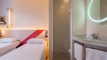 Habitación de hotel con dos camas, ducha, baño con lavamanos y espejo, y una pared de acento roja.
