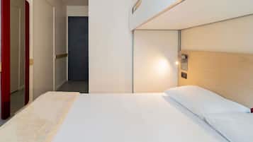 Habitación de hotel con una cama, cabecera de madera, mesita de noche y espejo con marco rojo.