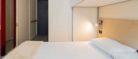 Habitación de hotel con una cama, cabecera de madera, mesita de noche y espejo con marco rojo.