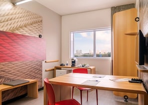 Enjoy city views from the large window in this stylish room, featuring a desk, chair, and kitchenette.