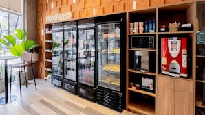 A counter area with a refrigerated display, a coffee machine, and a seating area with a plant. - ibis budget Sao Paulo Paulista (São Paulo)