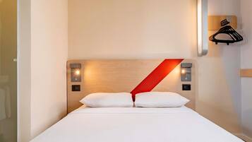 Camera d'albergo con un letto, una testiera in legno, un dettaglio rosso, luci a parete e un appendiabiti.