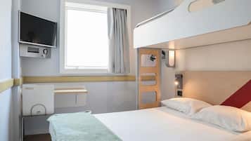 Uma cama beliche com uma televisão acima, uma janela com cortinas e uma mesa de cabeceira com tomada.