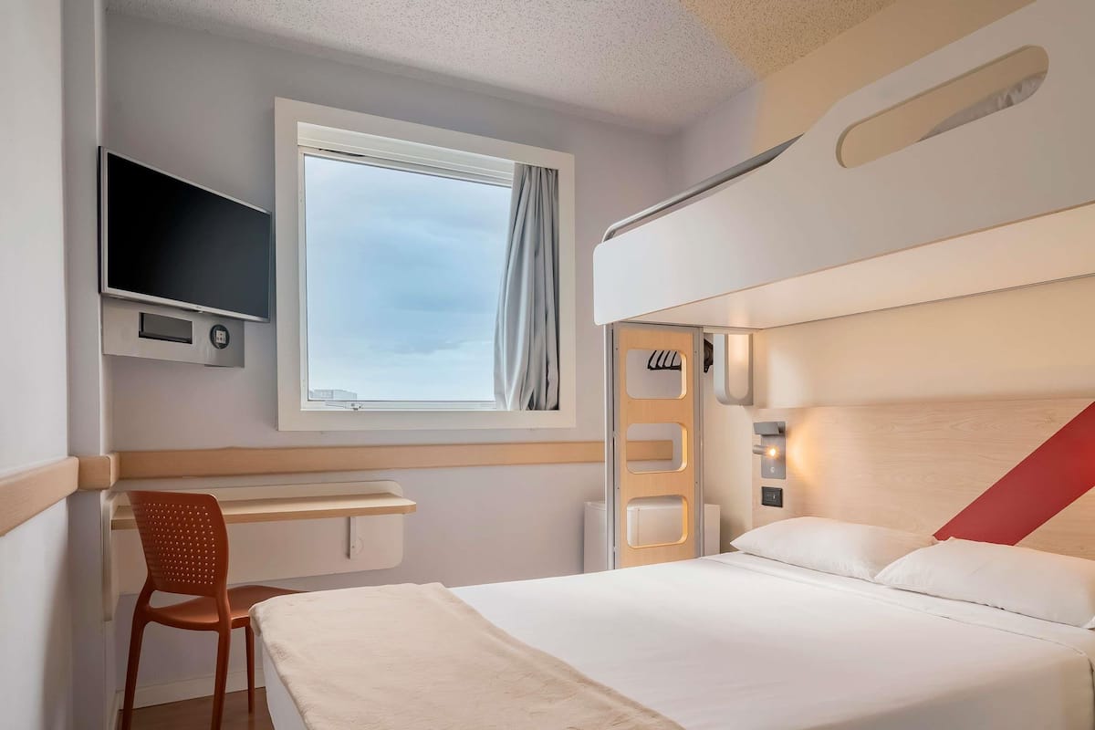 A hotel room with a bed, a desk, a chair, a TV, and a window with curtains.